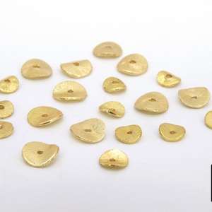 May include: A collection of 18 gold-toned metal beads with a hole in the center. The beads are shaped like a half-circle and have a textured surface.
