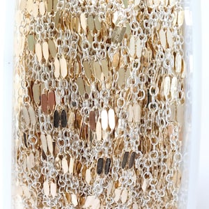 May include: A roll of gold-colored chain with silver-colored links and flat, oval-shaped gold accents. The chain is tightly wound and appears to be new. The image is well-lit, showing the chain's texture and shine. The product is likely for jewelry making.