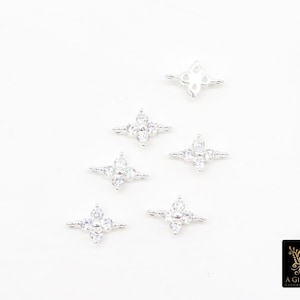 May include: Silver-coloured jewellery components with a four-petal flower design, each set with clear, sparkling gemstones. The components are arranged on a white surface. The logo "A Girls Gems" is in the bottom right corner.