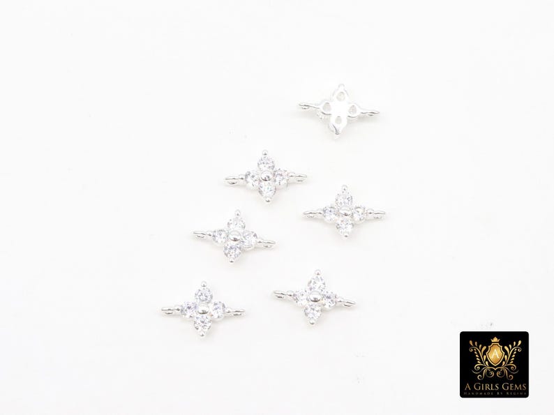 May include: Silver-coloured jewellery components with a four-petal flower design, each set with clear, sparkling gemstones. The components are arranged on a white surface. The logo "A Girls Gems" is in the bottom right corner.
