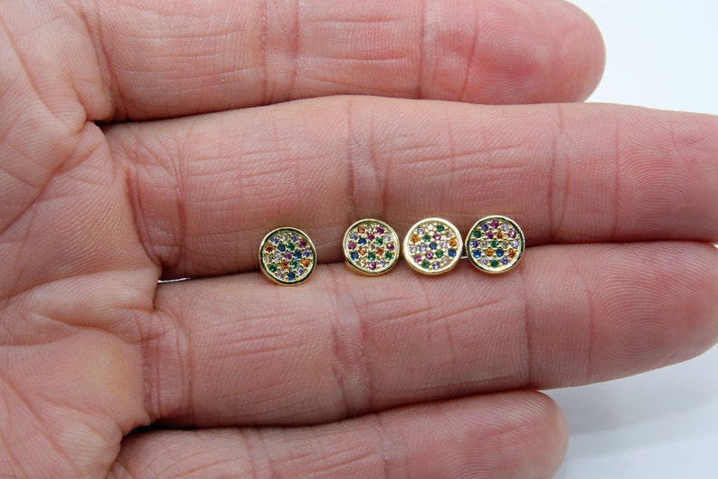 May include: Four gold-toned stud earrings with a round shape and a colorful, multi-faceted design. Each earring is set with small, round stones in various colors, including red, blue, green, and yellow.