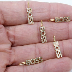 May include: Five gold-tone charms with the word "BOSS" spelled out in clear cubic zirconia stones. The charms are on a hand.