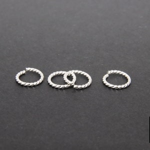 Pode incluir: Quatro argolas de salto torcidas de prata, cada uma com aproximadamente 1,25 cm de di&acirc;metro, sobre um fundo preto.