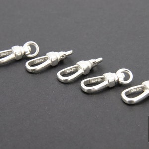 May include: Five silver-toned metal swivel clasps, each with a loop on one end and a hook on the other. The clasps are arranged in a row on a black surface.