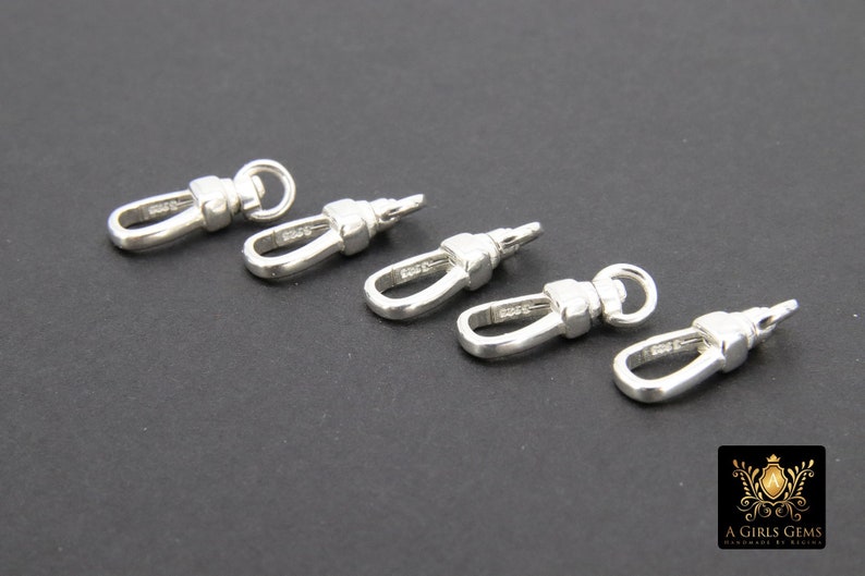 May include: Five silver-toned metal swivel clasps, each with a loop on one end and a hook on the other. The clasps are arranged in a row on a black surface.