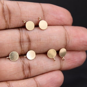 May include: Six gold-colored metal circles with a small loop on the top. The circles are flat and smooth.