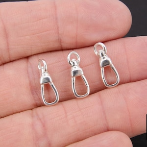 May include: Three silver-toned metal swivel clasps, also known as lobster clasps, are shown on a hand. The clasps are about 1 inch long.