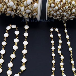 May include: Two spools of gold chain with white round beads. The chain is strung with small round beads that are white with a gold rim.