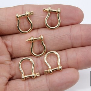 Puede incluir: Cinco cierres en forma de U de metal de color dorado con cierre de tornillo. Los cierres están dispuestos en una mano.