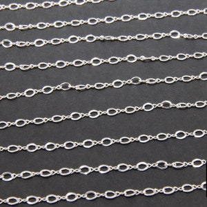 May include: A close-up of a silver chain with oval links. The chain is laid out in rows on a black surface.