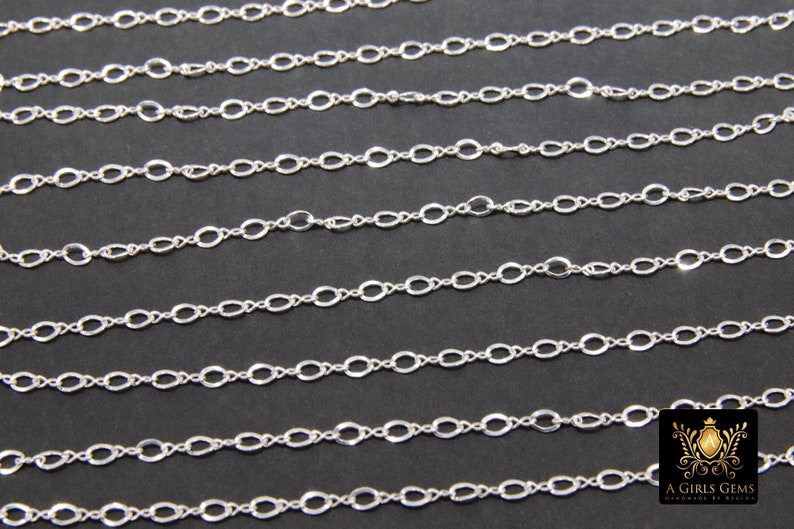 May include: A close-up of a silver chain with oval links. The chain is laid out in rows on a black surface.