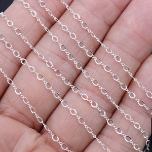 May include: Multiple strands of silver chain, featuring a delicate oval link design. The chain is displayed on a hand, showcasing its length and flexibility.