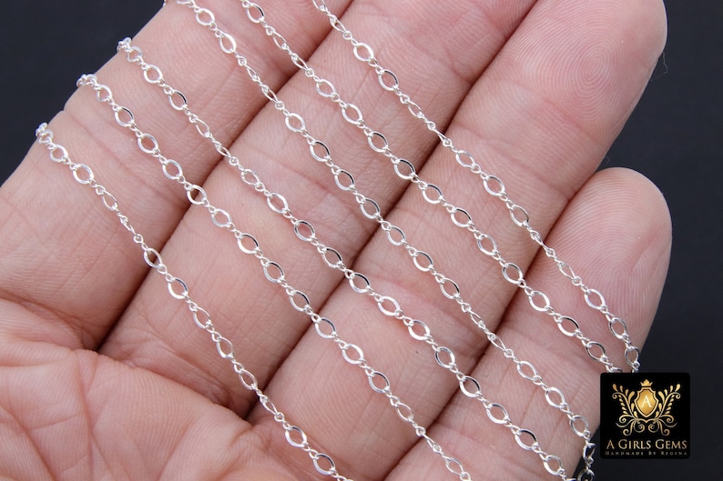May include: Multiple strands of silver chain, featuring a delicate oval link design. The chain is displayed on a hand, showcasing its length and flexibility.