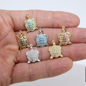 Op de afbeelding: Vijf gouden schildpadbedels met verschillende gekleurde kristallen accenten. De bedels zijn bezet met blauwe, turquoise, rode, heldere en witte kristallen.