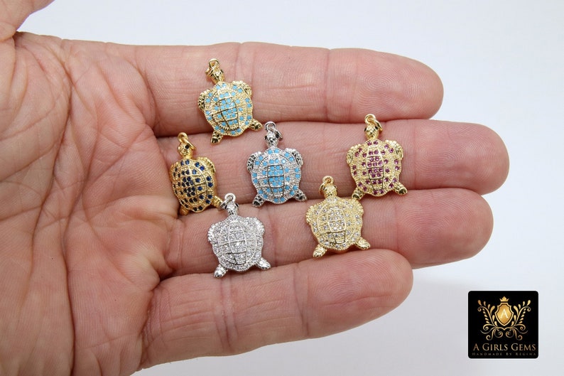 Op de afbeelding: Vijf gouden schildpadbedels met verschillende gekleurde kristallen accenten. De bedels zijn bezet met blauwe, turquoise, rode, heldere en witte kristallen.