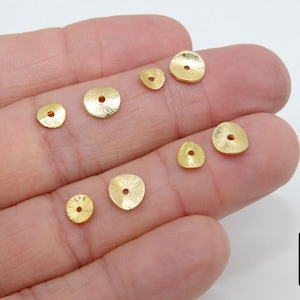 May include: Assortment of gold-toned metal round disc beads with a hole in the center. The beads are of varying sizes and are displayed on a hand.