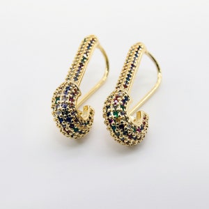 May include: A pair of gold-tone earrings with a safety pin design. The earrings are decorated with colorful cubic zirconia stones.