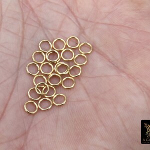 May include: A pile of 20 gold jump rings, approximately 5mm in diameter, on a person's hand.