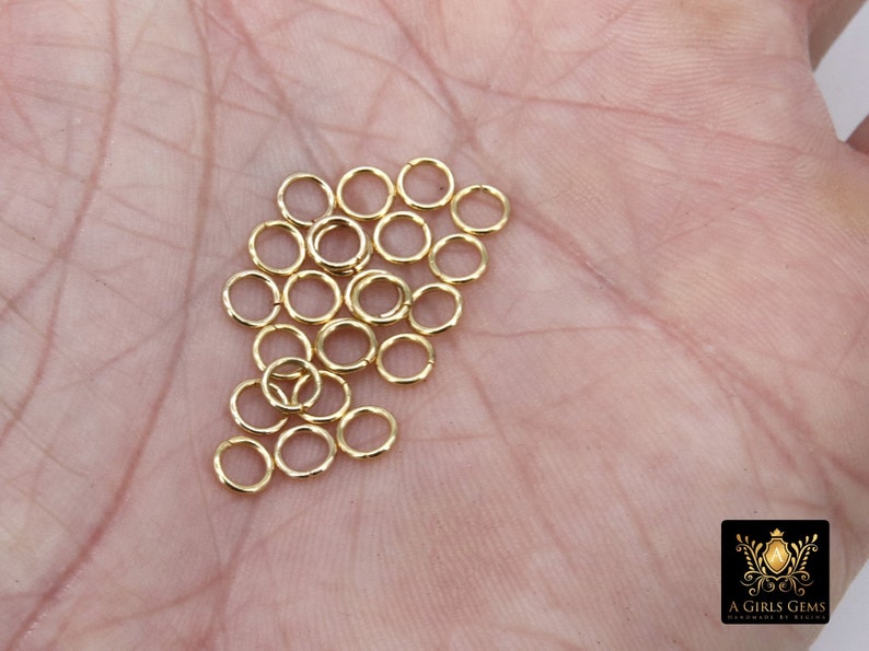 May include: A pile of 20 gold jump rings, approximately 5mm in diameter, on a person's hand.