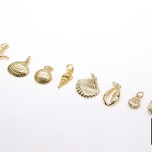 May include: A set of nine gold-coloured charms featuring various seashell designs, including a starfish, a conch shell, and a clam shell.