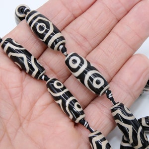 May include: A string of black and white agate beads with a repeating pattern of circles. The beads are strung on a black cord.