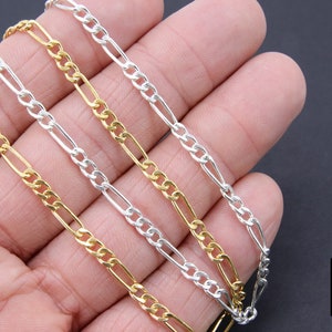 May include: Three gold and silver chains, a gold chain, a silver chain, and a silver chain with a gold accent, are displayed on a hand. The chains are all the same style, a figaro chain.