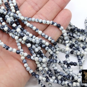 May include: A strand of black and white speckled round beads. The beads are approximately 4mm in diameter and are strung on a clear thread.