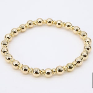 May include: A gold beaded bracelet with a simple design. The beads are round and have a slightly textured surface.