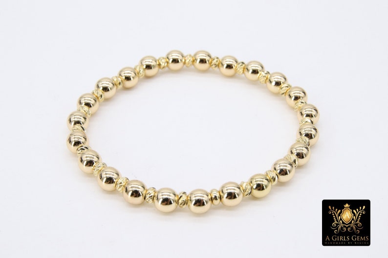 May include: A gold beaded bracelet with a simple design. The beads are round and have a slightly textured surface.