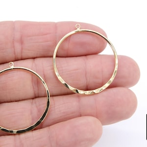 May include: Two gold-toned hammered metal hoops with a jump ring at the top. The hoops are approximately 2 inches in diameter.