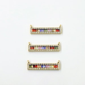 Puede incluir: Tres colgantes de barra de oro con un arcoíris de cristales baguette coloridos engastados en un marco de cristal transparente.