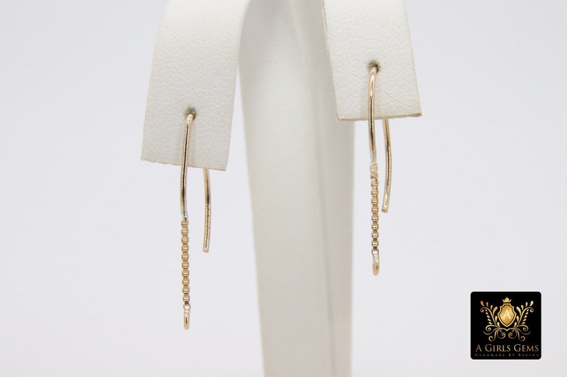 Pu&ograve; includere: Un paio di orecchini pendenti in oro con un delicato design a catena. Gli orecchini sono su un espositore bianco.