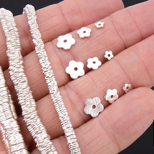 May include: Silver chain necklace with a textured, woven design. The chain is shown with a variety of silver flower-shaped beads in different sizes.