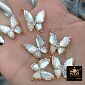 May include: Five gold butterfly charms with white iridescent wings and clear rhinestone accents. The charms have a loop at the top for attaching to jewelry.