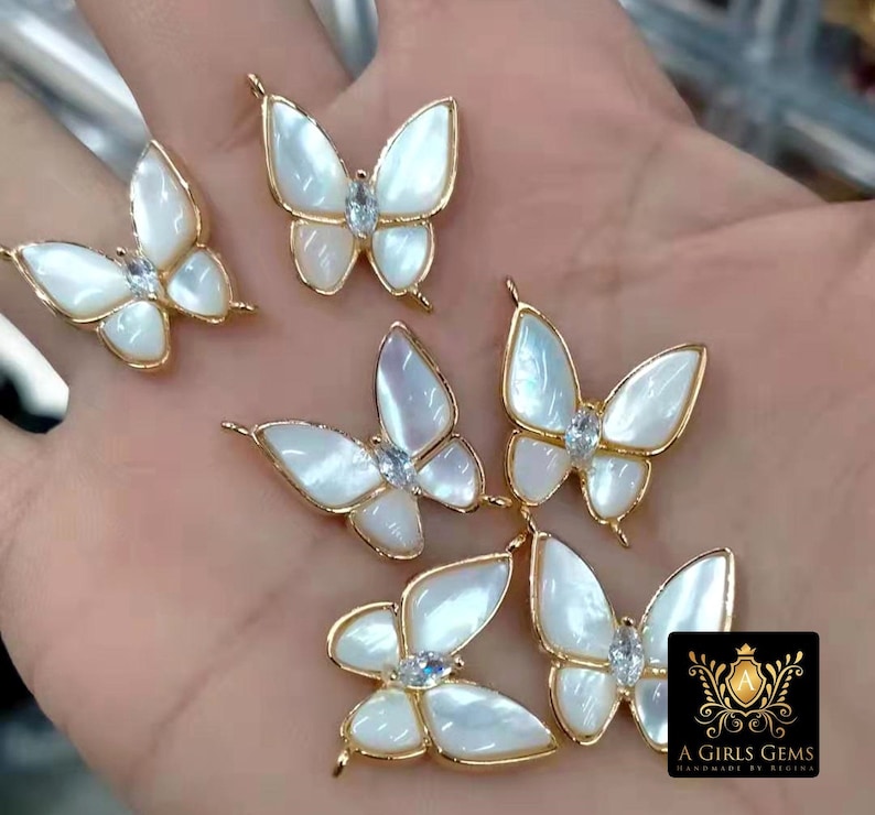 May include: Five gold butterfly charms with white iridescent wings and clear rhinestone accents. The charms have a loop at the top for attaching to jewelry.