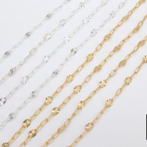 May include: Five strands of chain, two gold and three silver, with a textured, flower-shaped design on each link. The chains are laid out on a white surface.