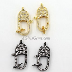 May include: Two pairs of gold and black metal clasps with clear crystal embellishments. The clasps are oval shaped and have a hook closure. AGirlsGems.com is printed on the white background.
