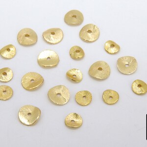 May include: A collection of 20 gold-toned metal beads with a textured surface. The beads are round with a hole in the center.