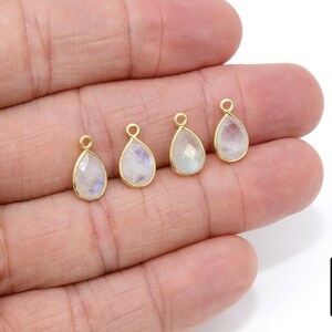 May include: Four gold-plated teardrop-shaped pendants with a white moonstone gemstone. Each pendant has a small loop at the top for attaching to jewelry.
