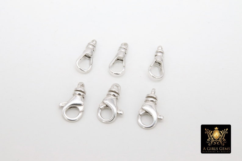 May include: Six silver-toned lobster clasps, each with a spring-loaded opening and a loop for attaching to a chain or cord.