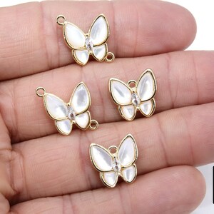 May include: Four gold butterfly charms with white enamel wings and clear rhinestone accents. The charms have a loop for attaching to jewelry.
