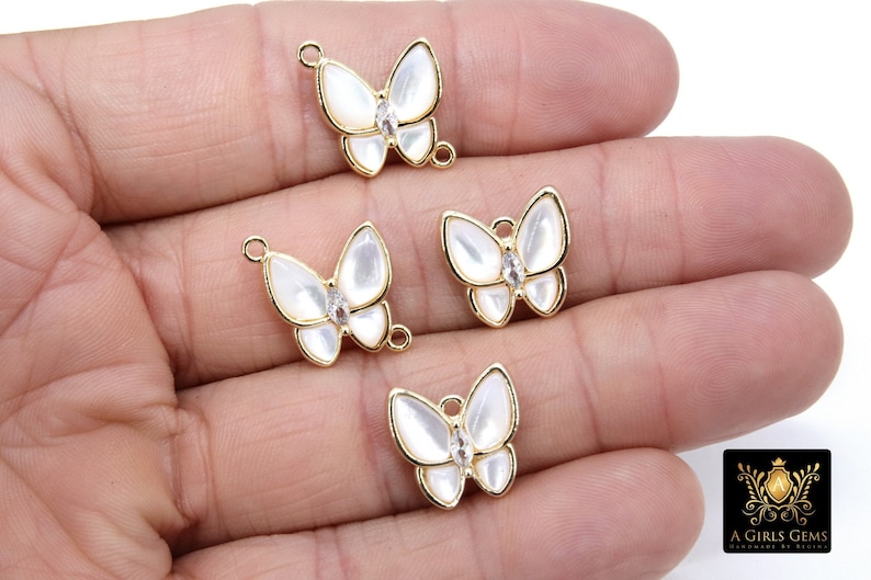 May include: Four gold butterfly charms with white enamel wings and clear rhinestone accents. The charms have a loop for attaching to jewelry.