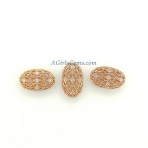 May include: Three rose gold oval beads with intricate openwork and small, sparkling white gemstones. The beads are arranged on a white background, showcasing their detailed design and elegant appearance. The website address "AGirlsGems.com" is visible.