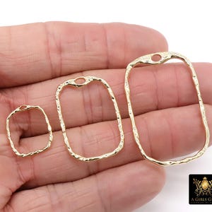 May include: Three gold-colored, open-frame rectangle charms with a textured surface. Each charm has a small hole at the top. The charms are in varying sizes, with the largest being approximately 1.5 inches long. The charms are displayed on a hand.