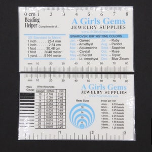 May include: A white plastic ruler with a black and white chart for bead sizes and wire gauge. The ruler has a black and white chart with the text "A Girls Gems Jewellery Supplies" and a chart of Swarovski birthstone colours.
