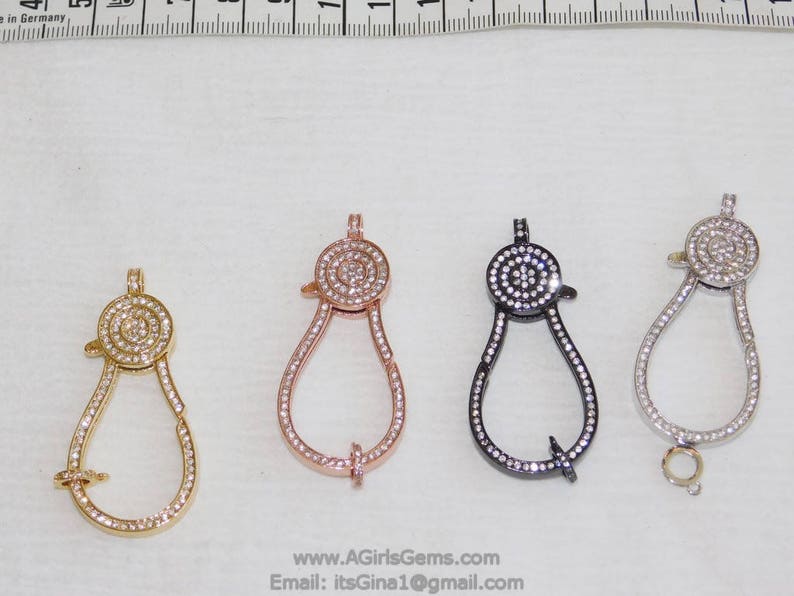 May include: Four different colored metal clasps with a round, clear crystal design. The clasps are in gold, rose gold, silver, and black.