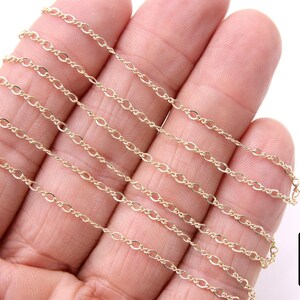 May include: A close-up of a gold chain necklace. The chain is made of small, oval-shaped links. The chain is laid out on a hand, showing the different lengths available.