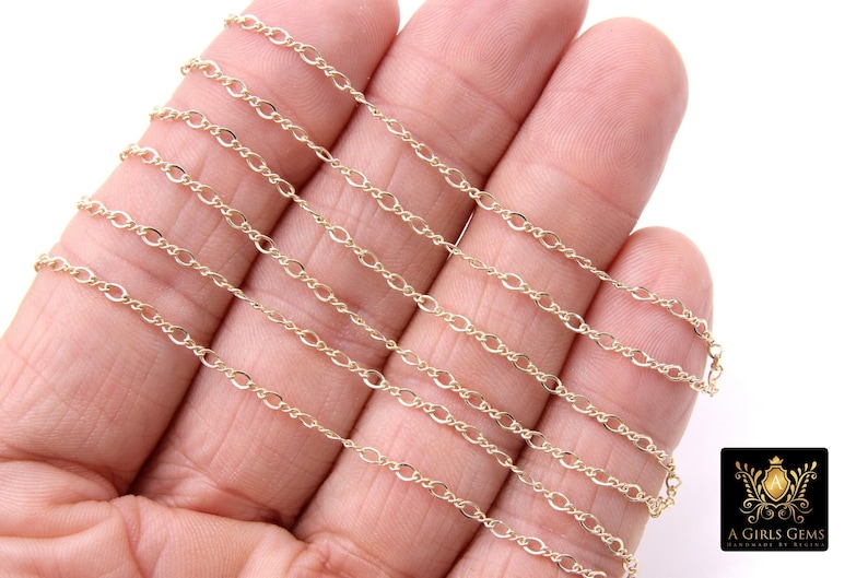 May include: A close-up of a gold chain necklace. The chain is made of small, oval-shaped links. The chain is laid out on a hand, showing the different lengths available.