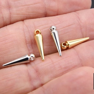 May include: Four metal cone-shaped charms with a loop at the top. Two charms are gold and two are silver.