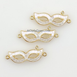 May include: Three gold-tone metal mask charms with white enamel and clear rhinestone accents. The masks are shaped like Venetian masquerade masks.